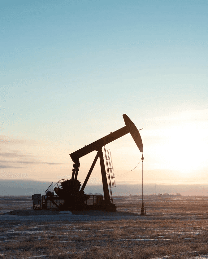 A silhouette of an oil rig on a plain with a sunset in the background