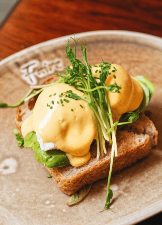 Eggs benedict with avocado and hollandaise on Faire branded plate, Eixample
