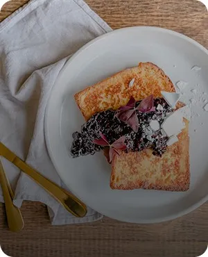 A plate with toasted bread topped with black beans, onions, and a dollop of cream, beside yellow utensils.
