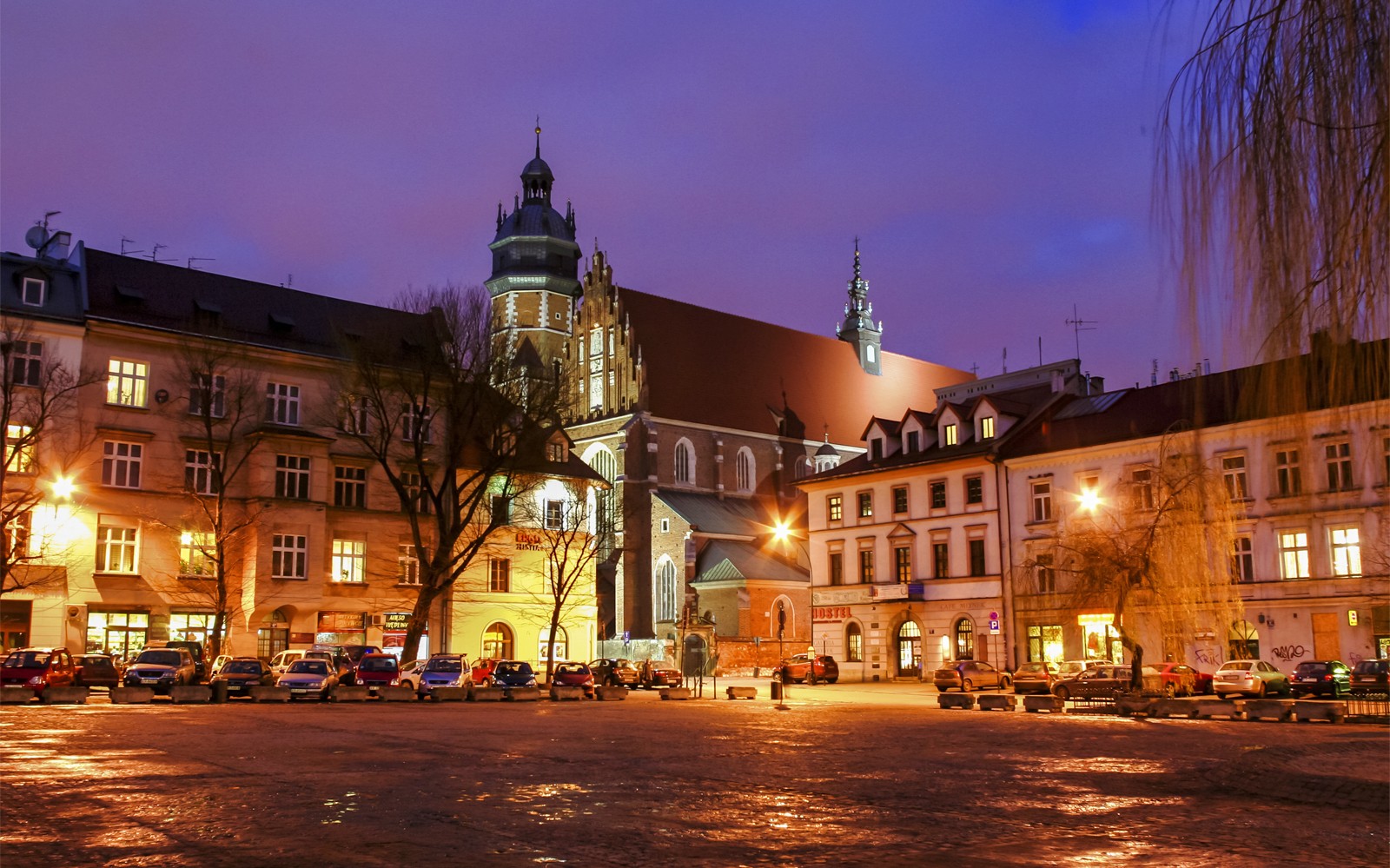 Krakau stadsplein bij schemering met verlichte historische gebouwen en kerktoren.