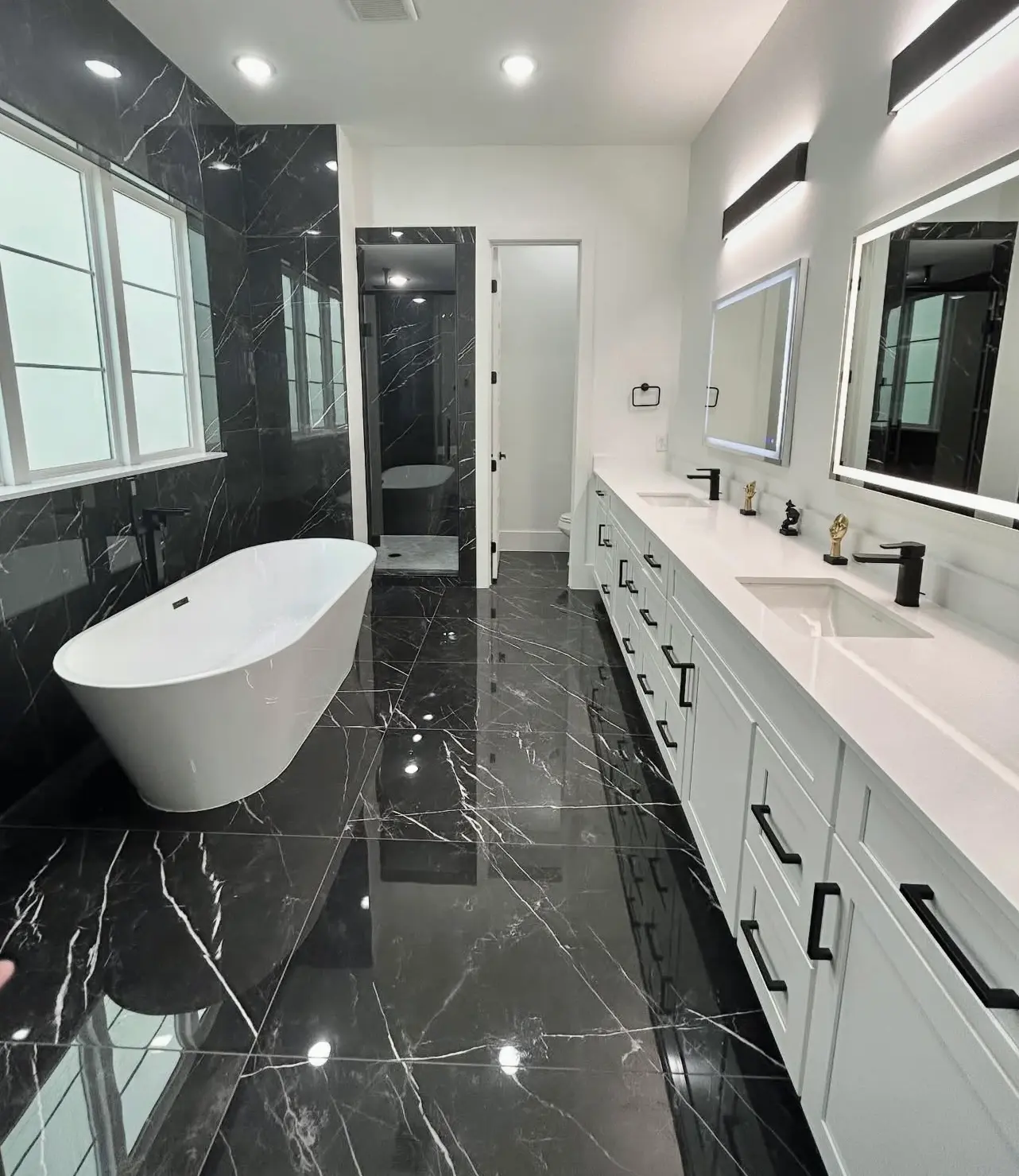 Modern master bathroom with a freestanding tub, clean black tiled floors, and white cabinetry after a professional deep clean.