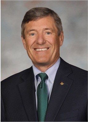 Young man in an orange hoodie and glasses at a desk with dual monitors in a dark office 