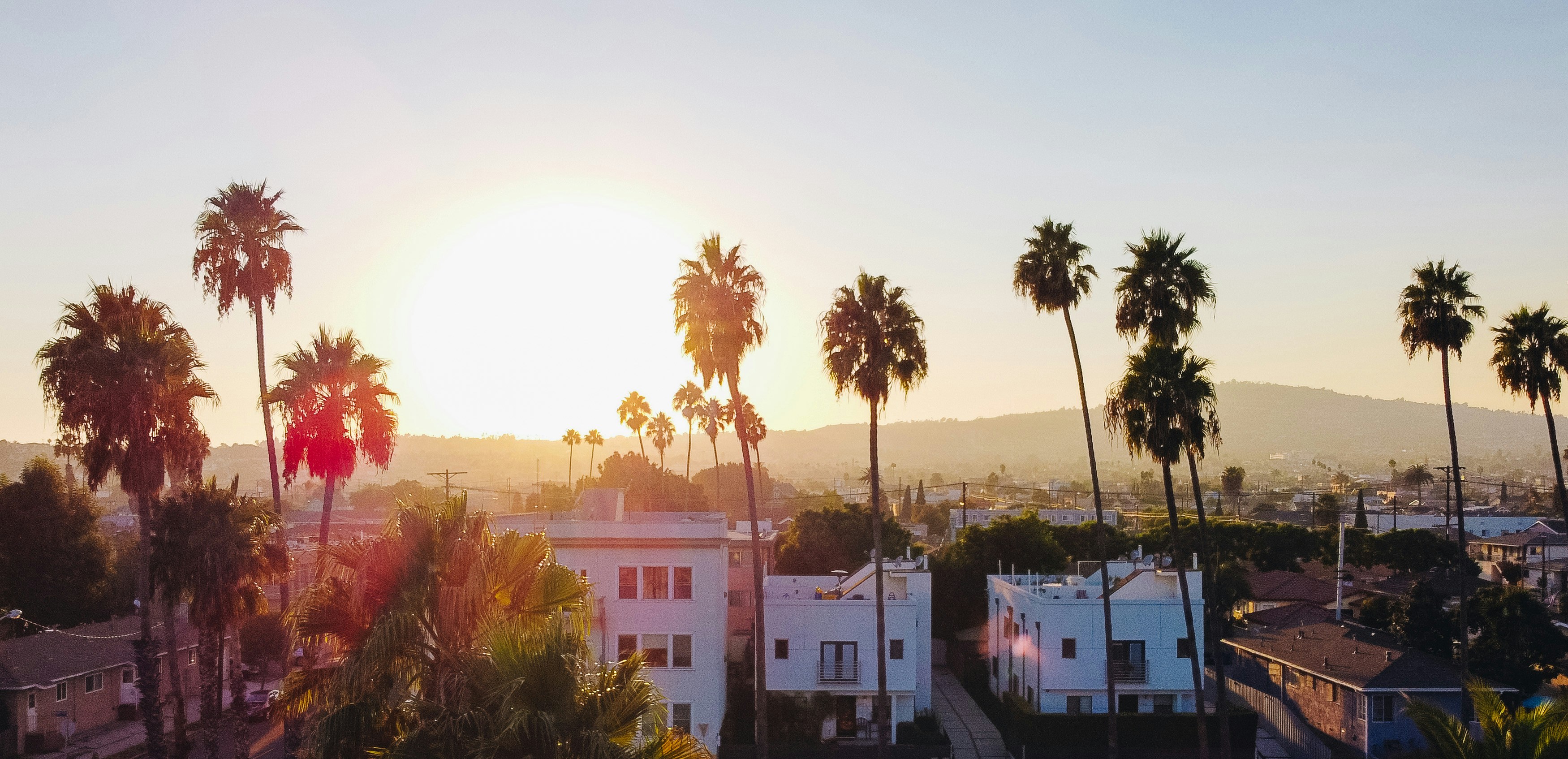Beautiful sunset over some mountiains,  with palm trees and some  million dollar homes in the foreground