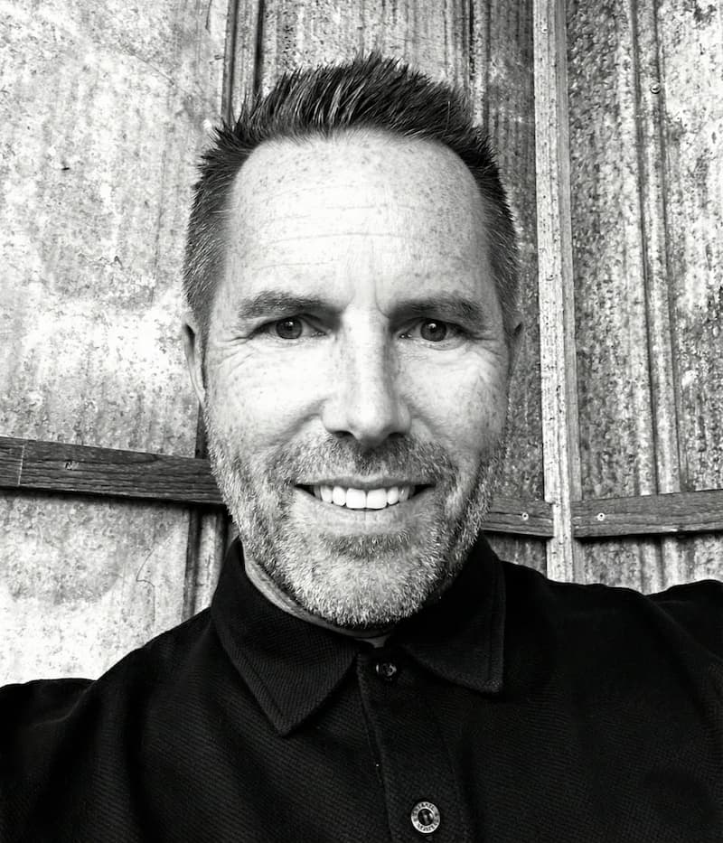 A smiling man in a suit and glasses sits at a table, with a modern office backdrop.