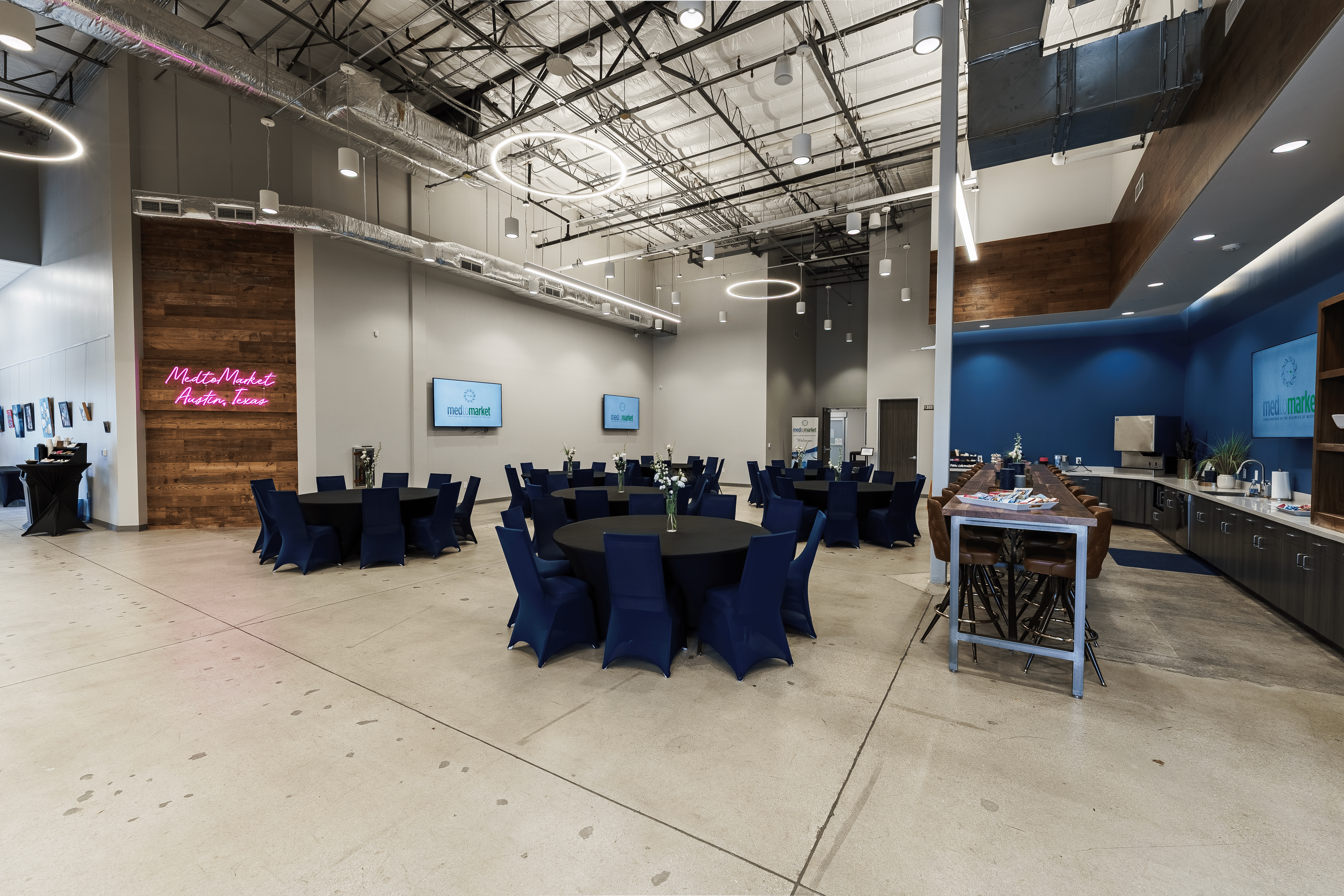 A young person with curly hair smiles at the camera while sitting in front of a laptop against a dark background.