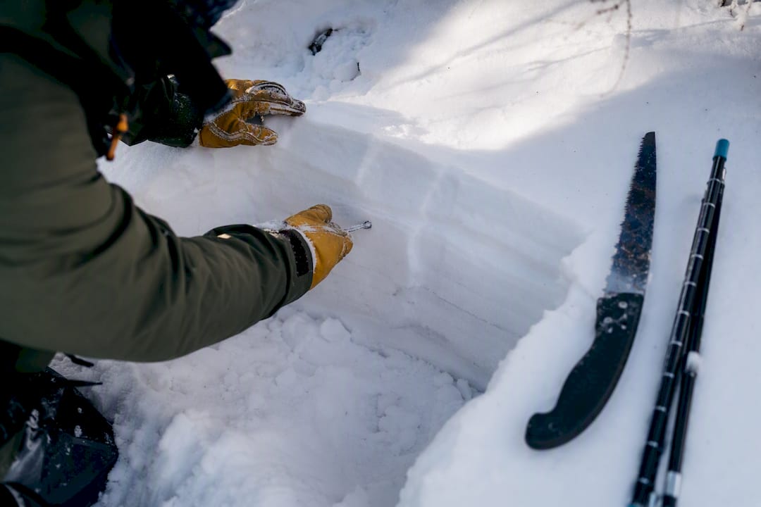 Gloved hands examining layers in mountain snow