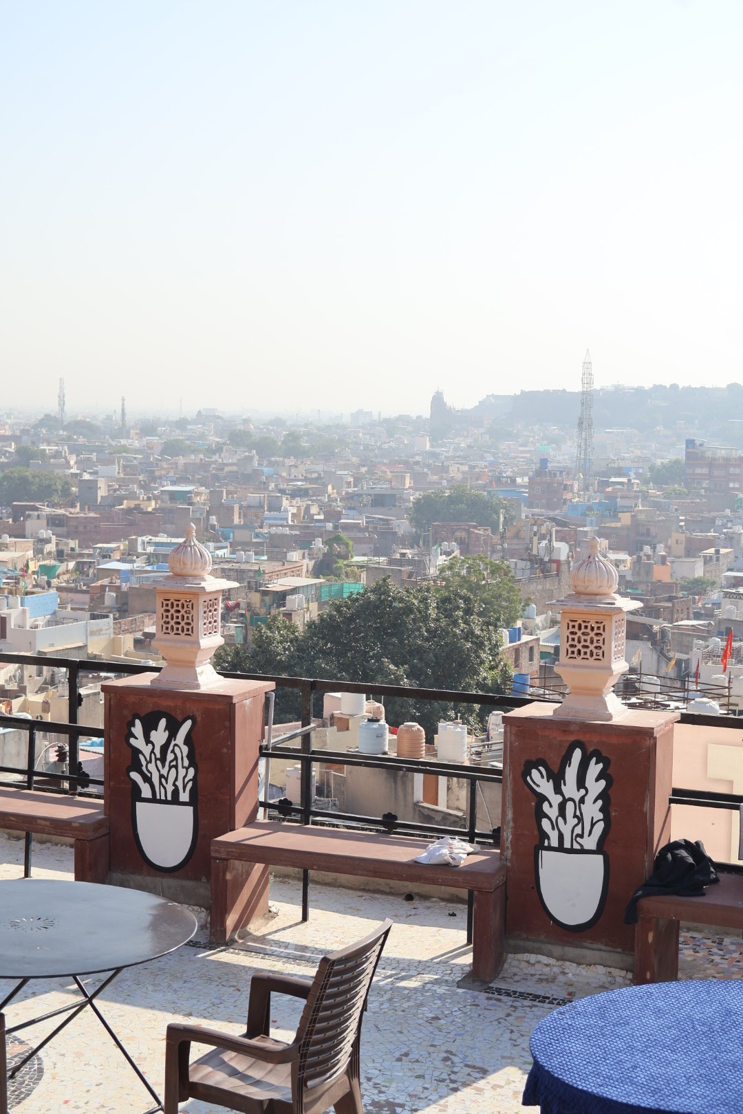 Mural painting showing potted plants painted in black-and-white on a brown terrace with restaurant tables visible and oriental decorations with Jodhpur skyline in the background