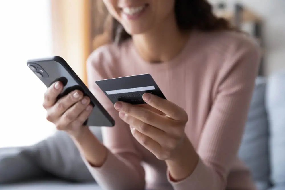 Smiling woman holding a smartphone and a credit card while making an online payment