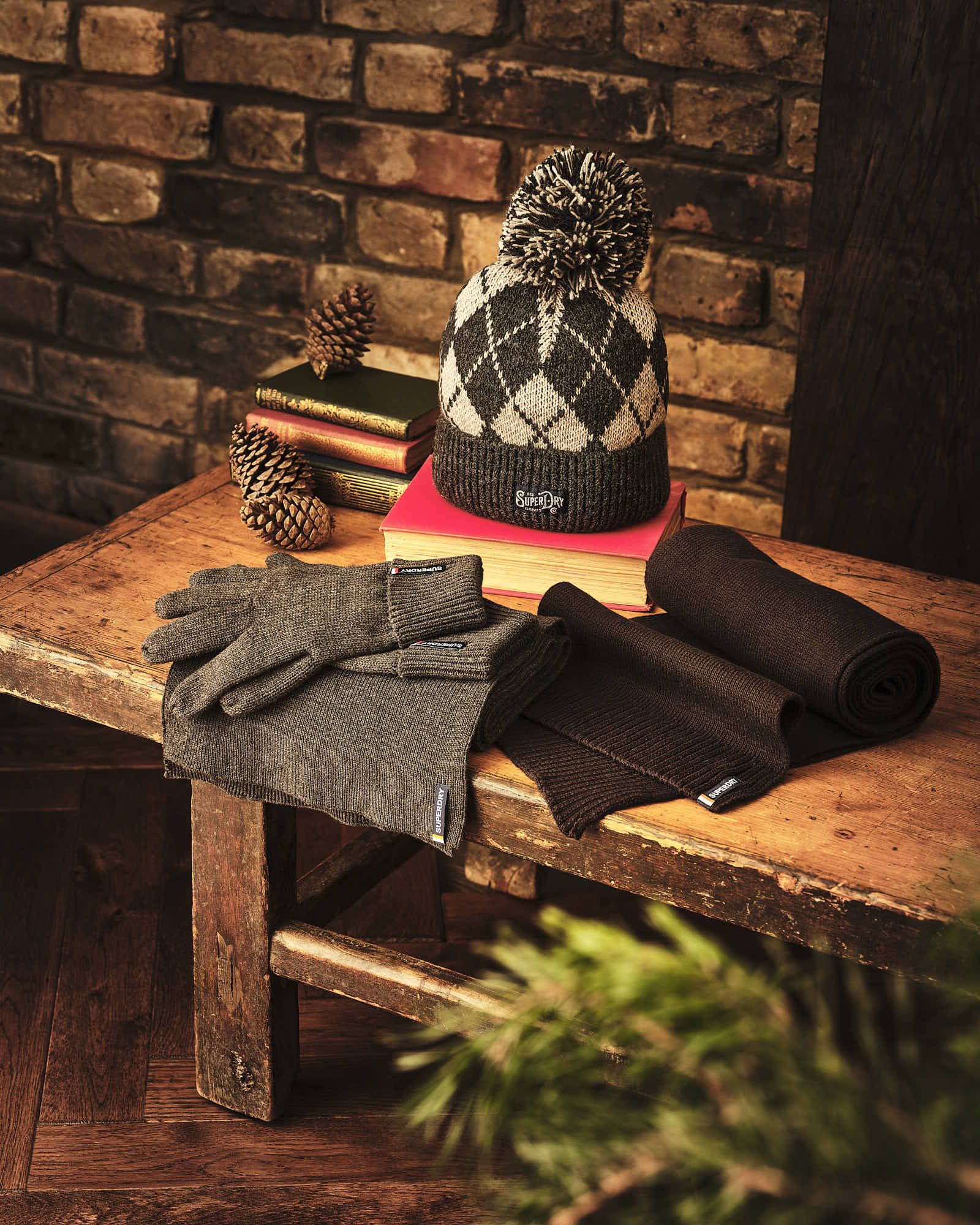 Cozy winter accessories including a knitted hat, gloves, and scarves on a rustic wooden bench with brick background.