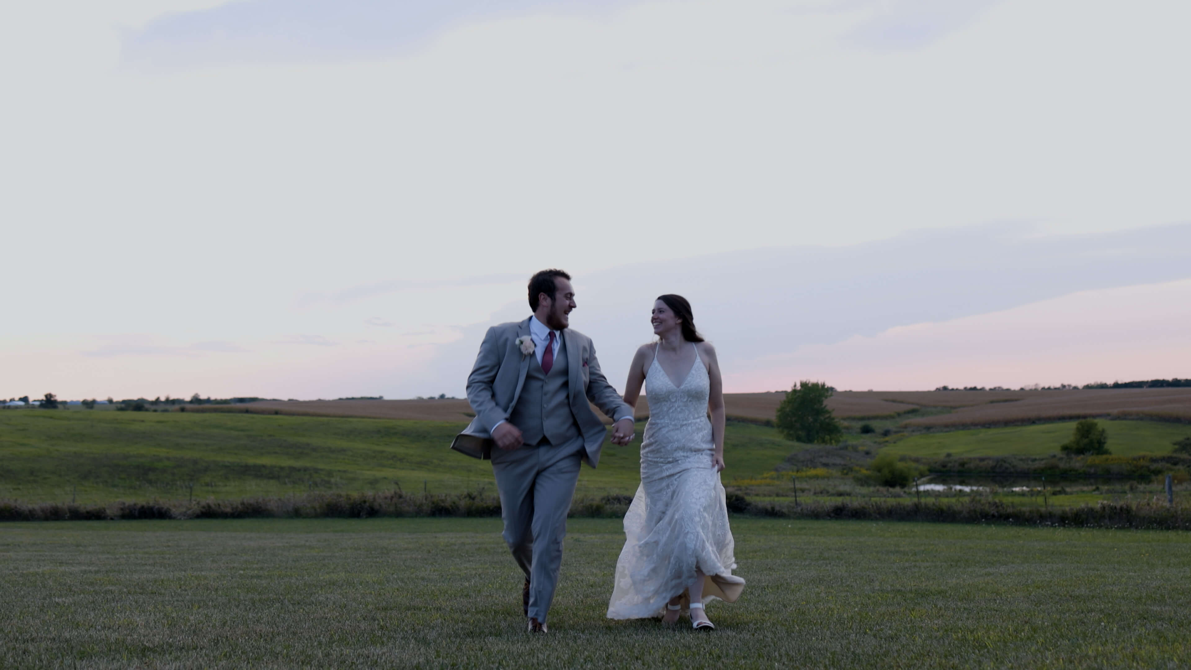 A bride and groom running in a field at sunset while looking at each other