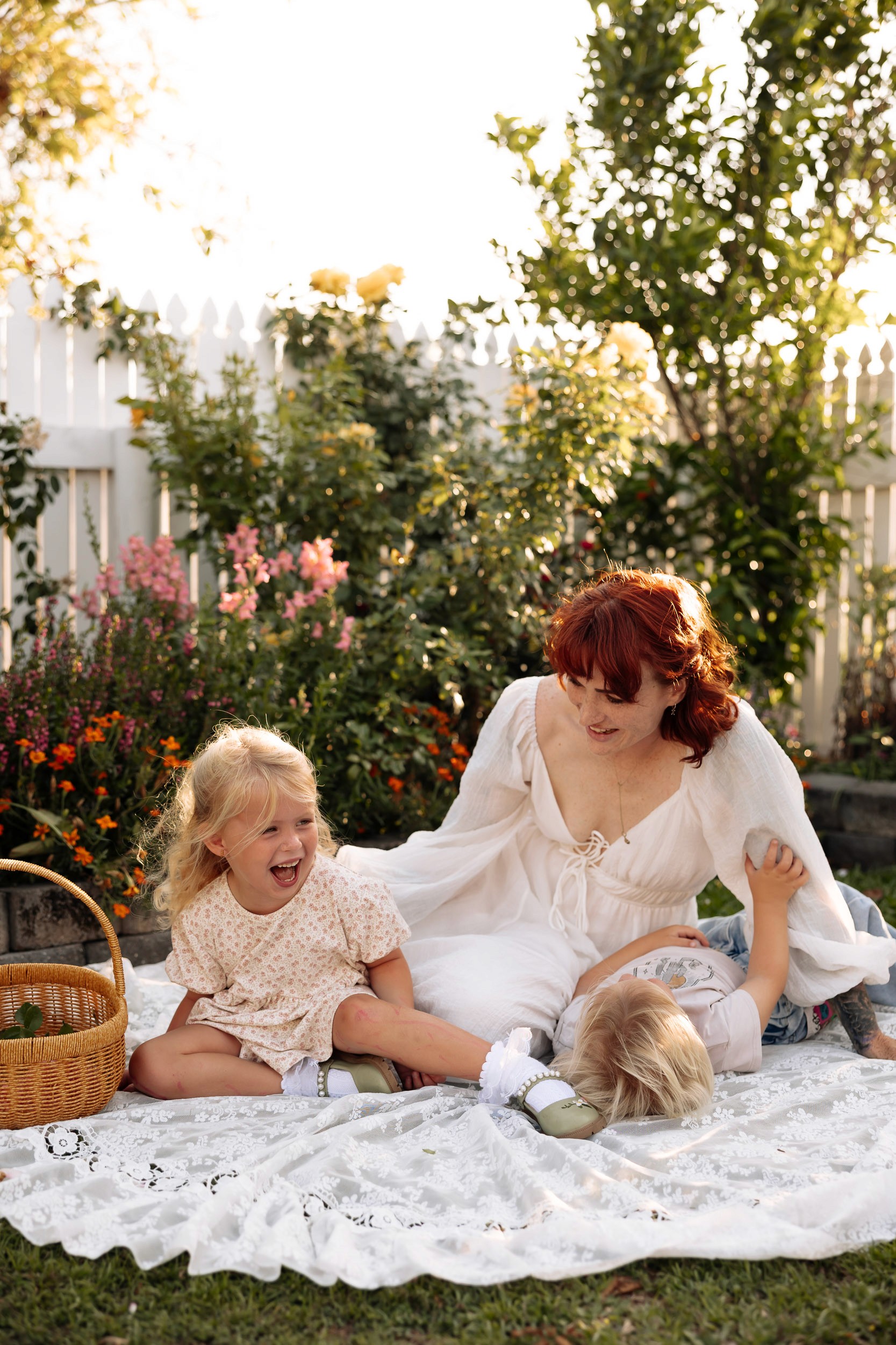 Mother cuddling her children on picnic blanket in cottage garden in home motherhood photoshoot in Mackay