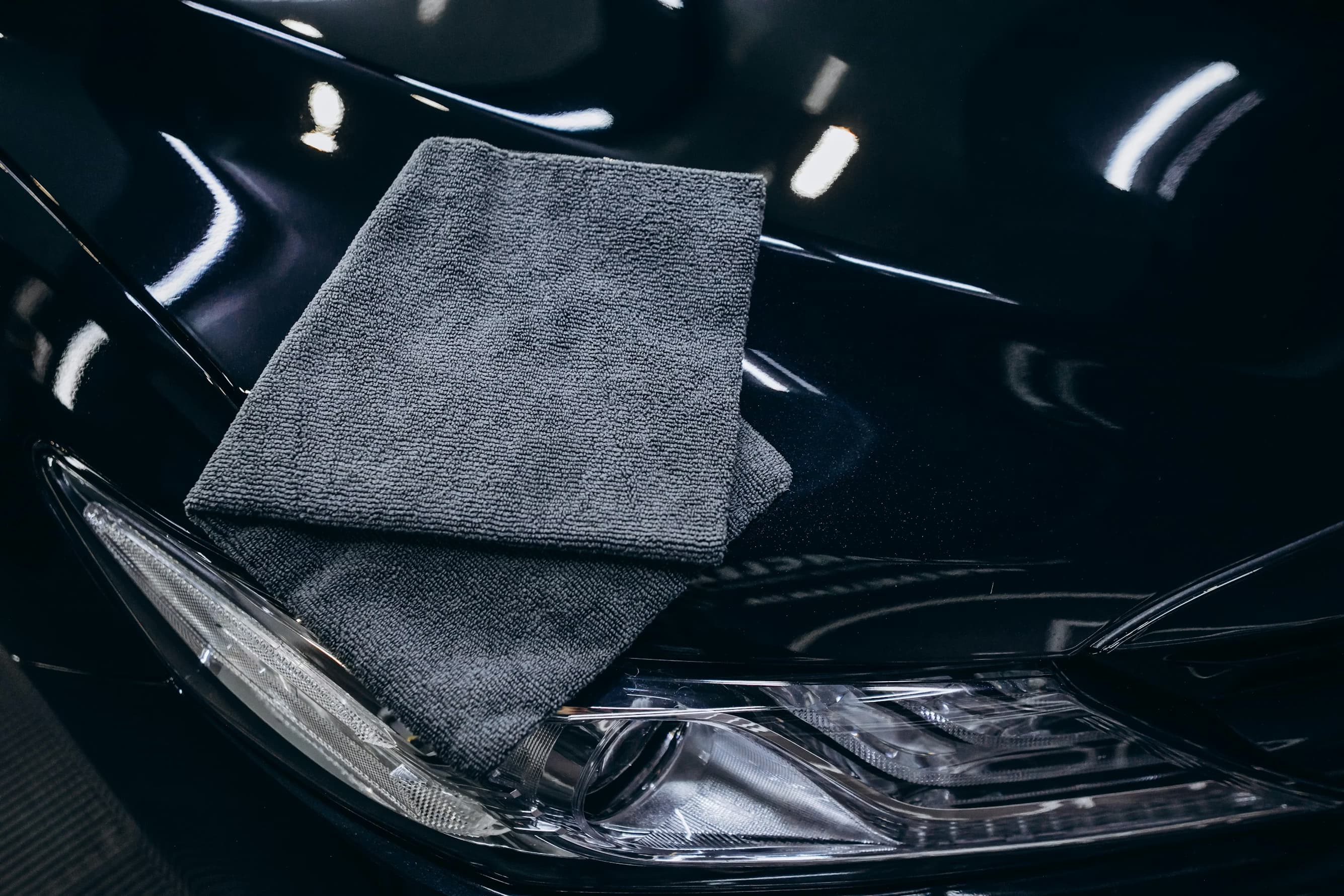 Microfibre posée sur la carrosserie noire d’une voiture lors d’un detailing automobile