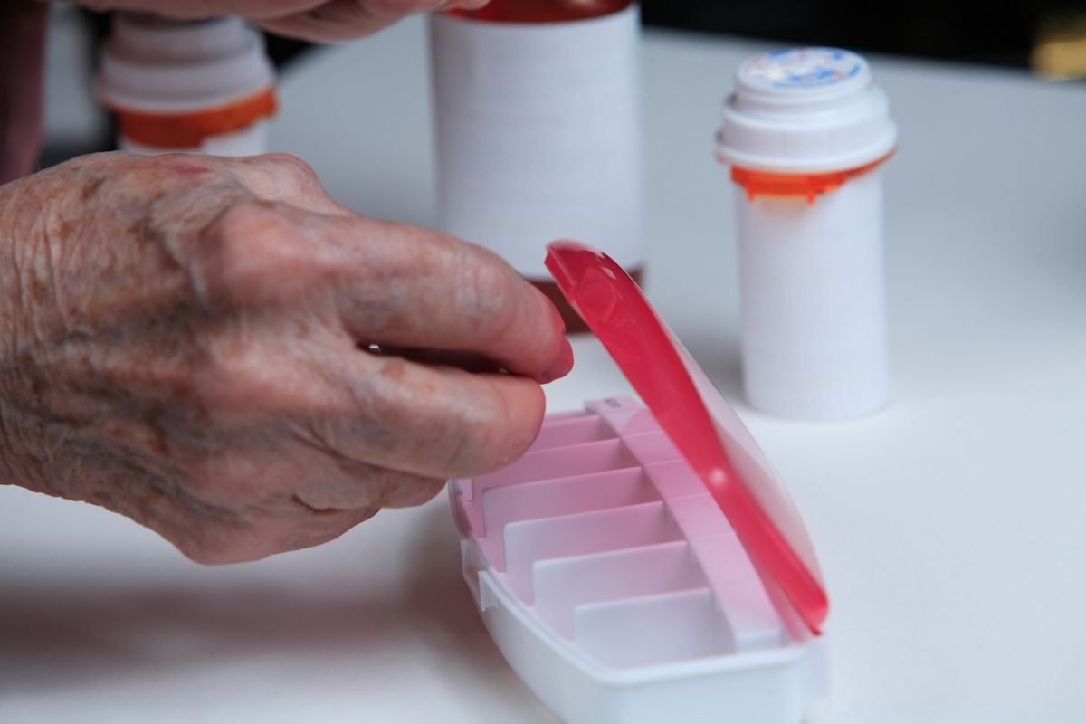 Elderly person placing medication in pill box.