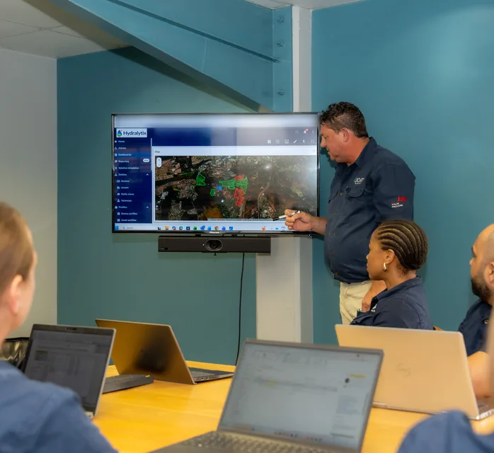 JOAT engineer presenting a Hydralytix network map to the team on a wall screen