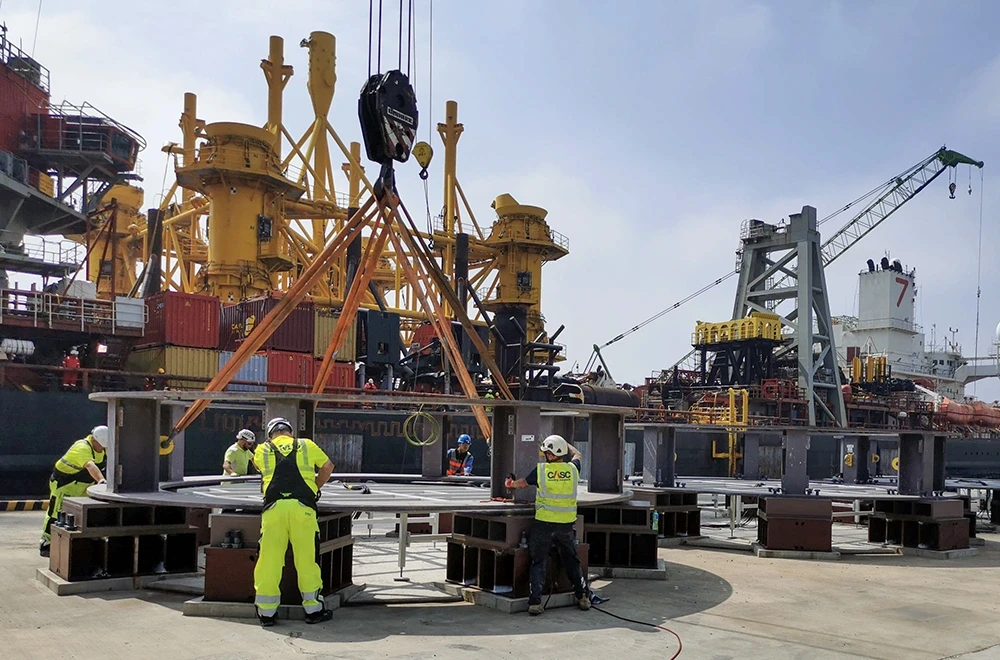 Offshore wind installation equipment on a marine construction platform, with workers in safety gear on deck.