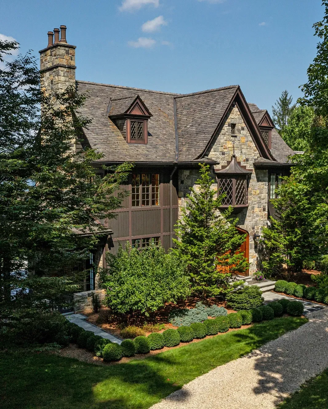 Rustic stone and wood house exterior with a steeply pitched roof, surrounded by lush greenery and trees.