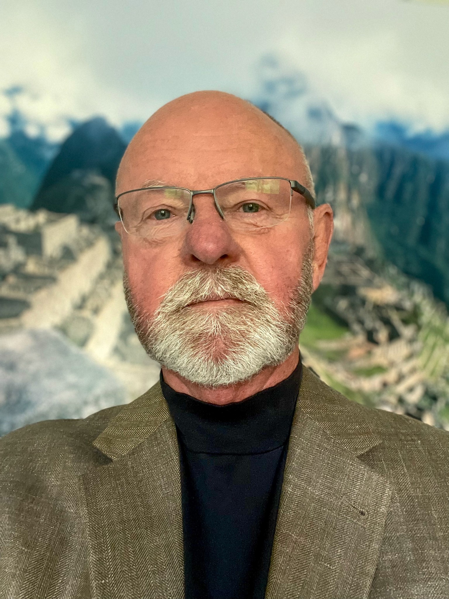 A young person with curly hair smiles at the camera while sitting in front of a laptop against a dark background.