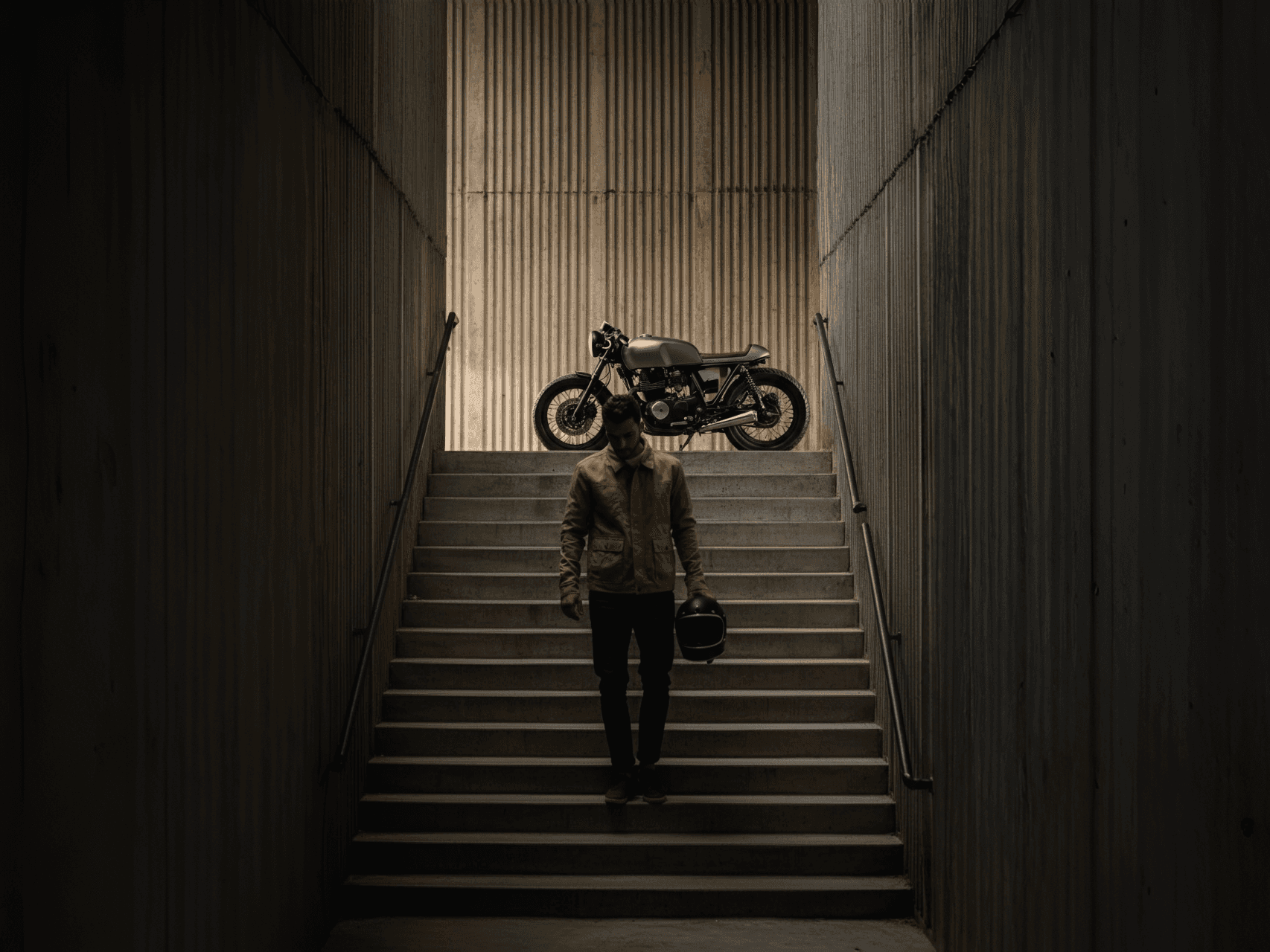 Man walking down the stair with a motorcycle on top of the stairs.