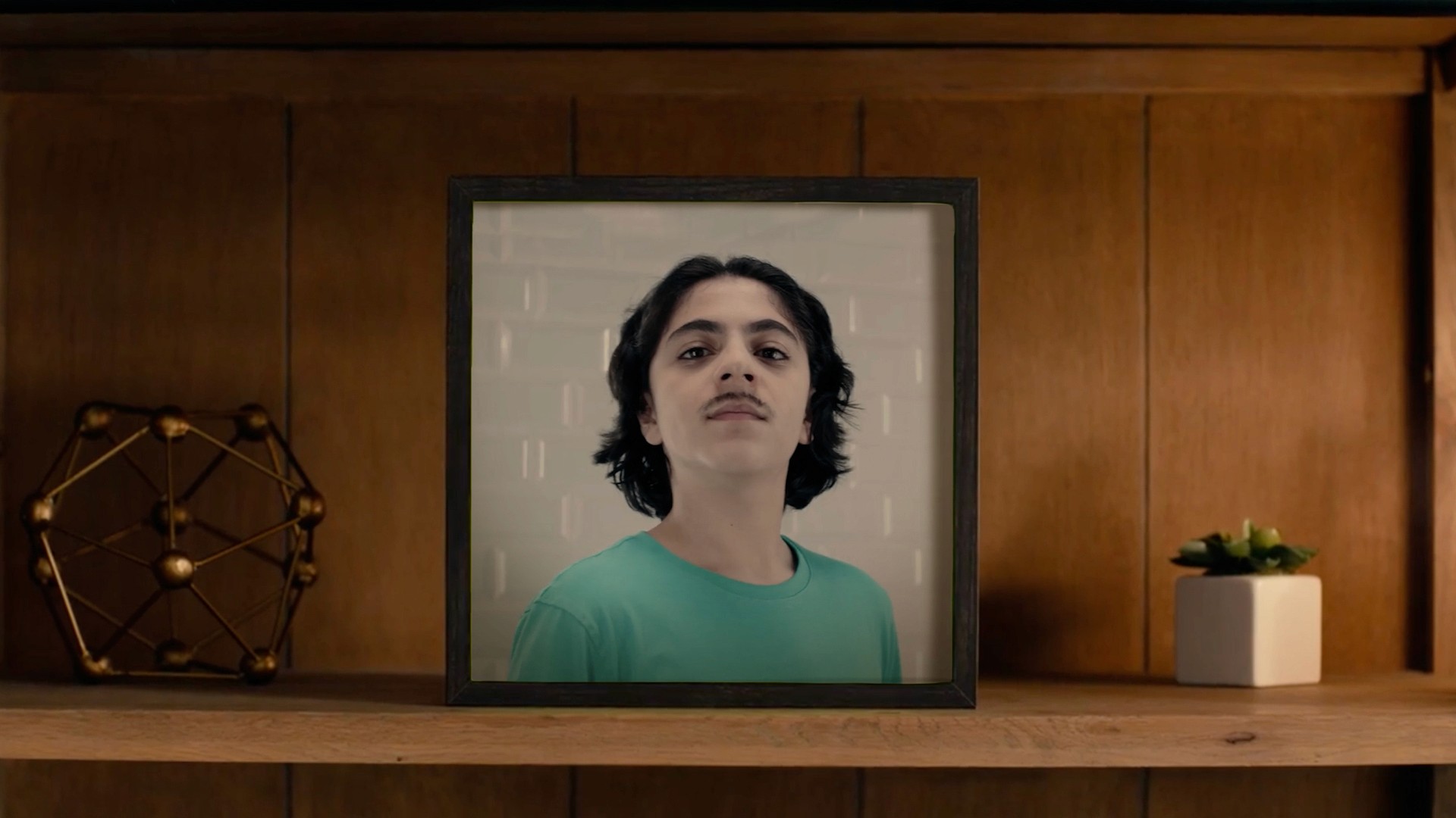 Close-up framed image of a teenage boy on a wooden shelf amongst other livingroom decoration