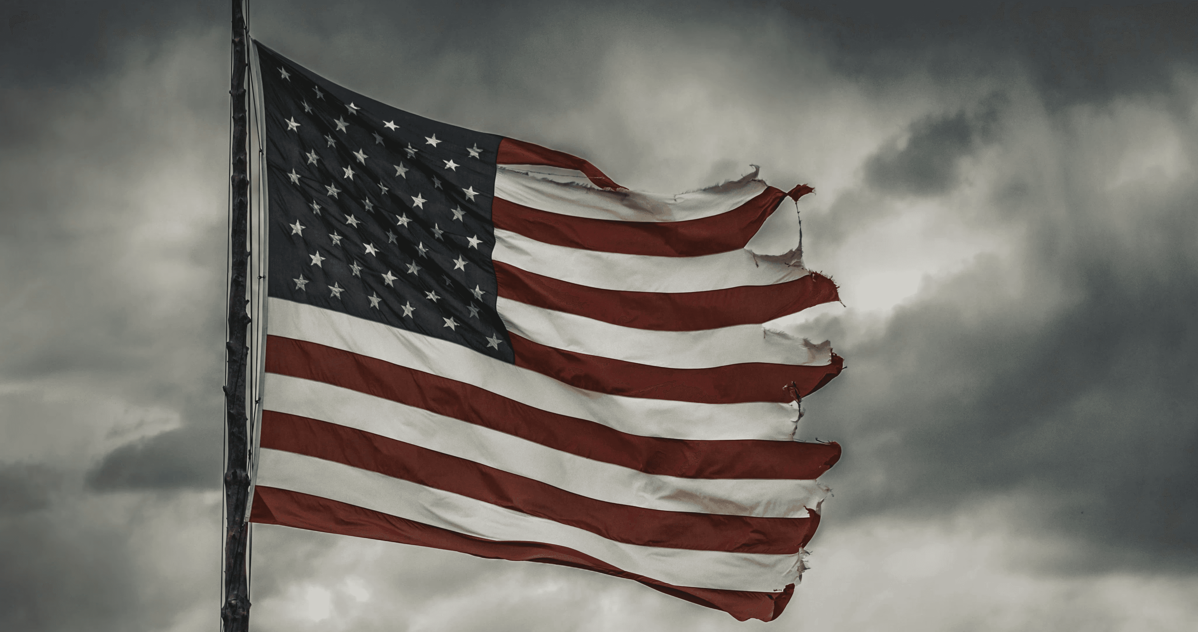 a large american flag flying in a cloudy sky