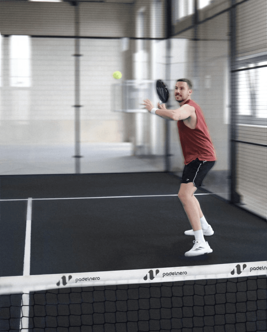 Padelspieler in rotem Shirt bereitet sich auf einen Schlag vor – volle Konzentration und Dynamik auf dem schwarzen Padelnero Court.