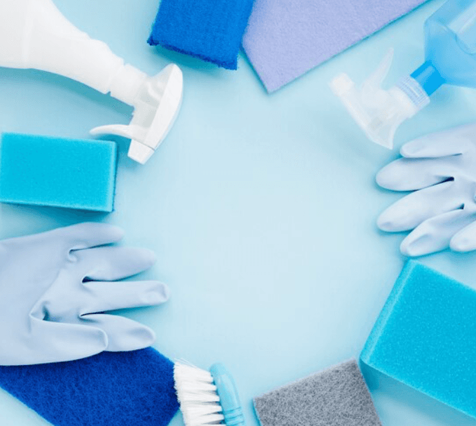 A young person with curly hair smiles at the camera while sitting in front of a laptop against a dark background.