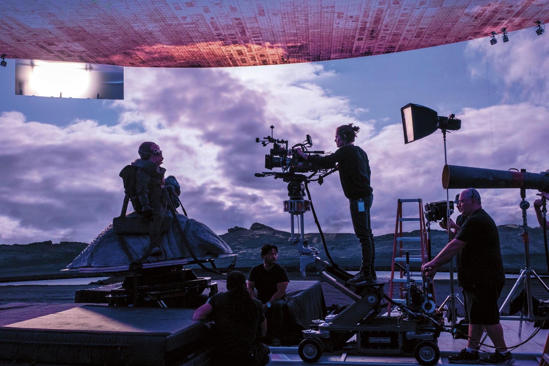 Silhouette of crew members working on a film set with dramatic clouds in the background at sunset.