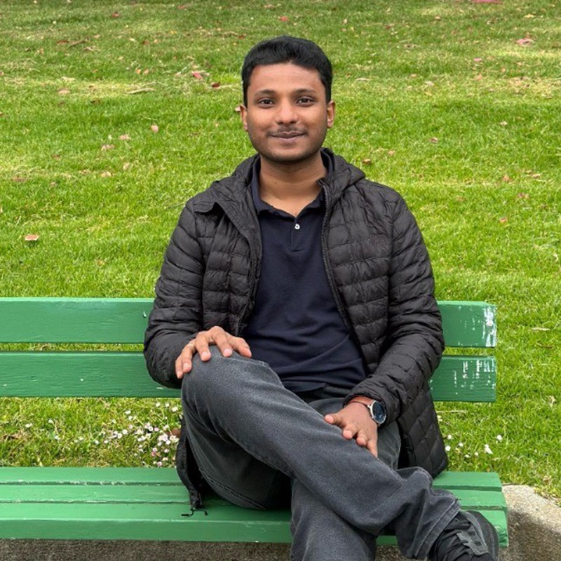 Navaneeth smiling, seated on a park bench, relishing a sunny afternoon.