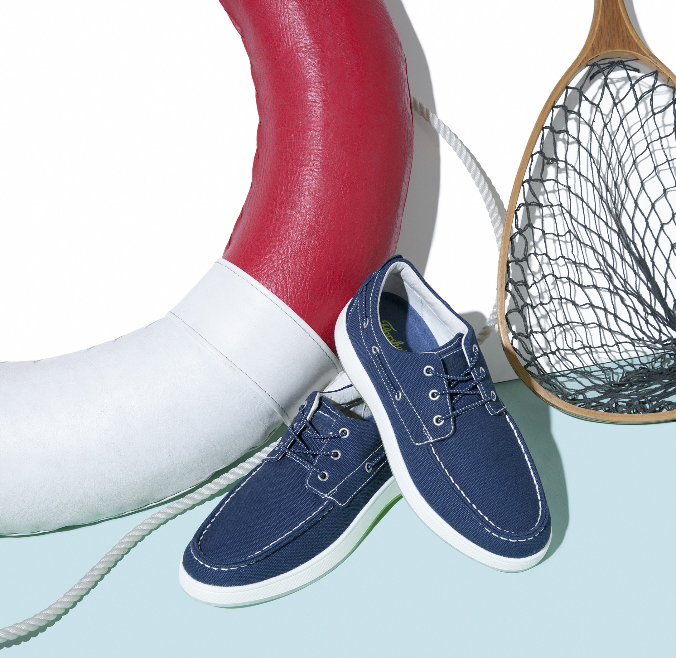 Nautica blue boat shoes from Florsheim Shoes styled with a red lifebuoy and fishing net for a nautical-themed display.