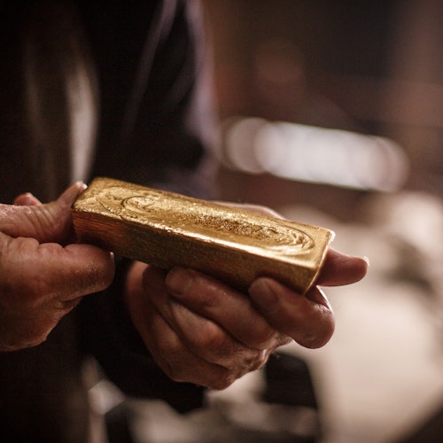 在昏暗的环境中，特写镜头展示了一双手握着金条。