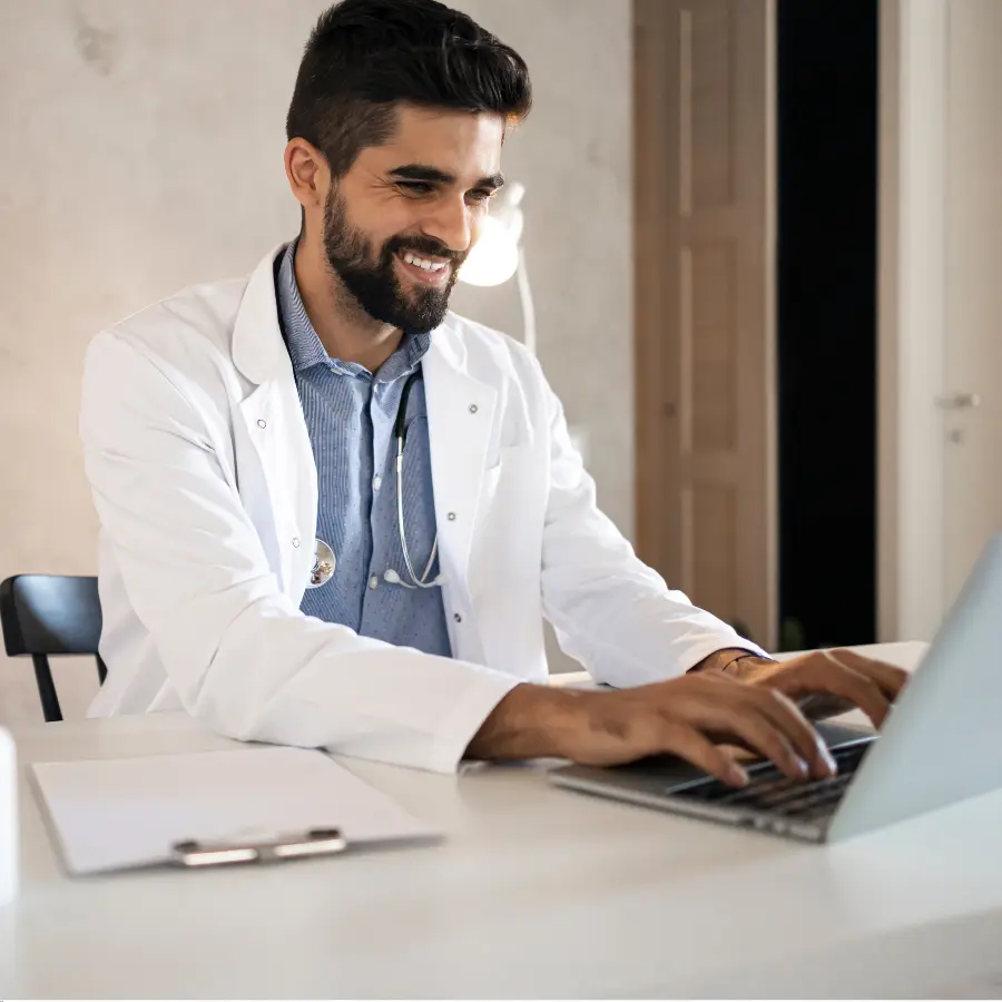 AI scribe technology assists a smiling doctor in a white coat as he types on a laptop in a modern office