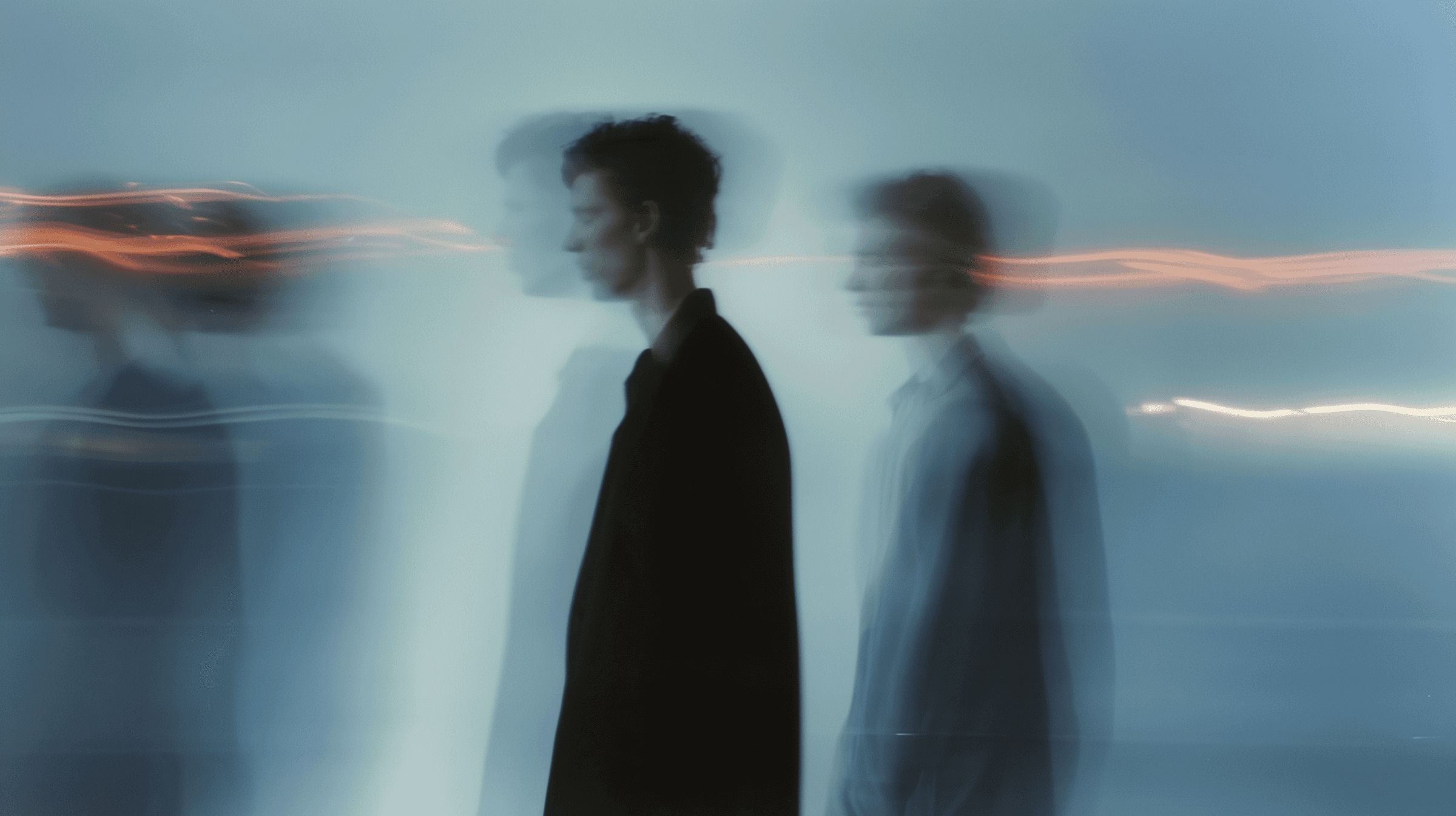 Few people with motion blur and orange light streaks on a pale blue background, slow shutter speed double exposure effect