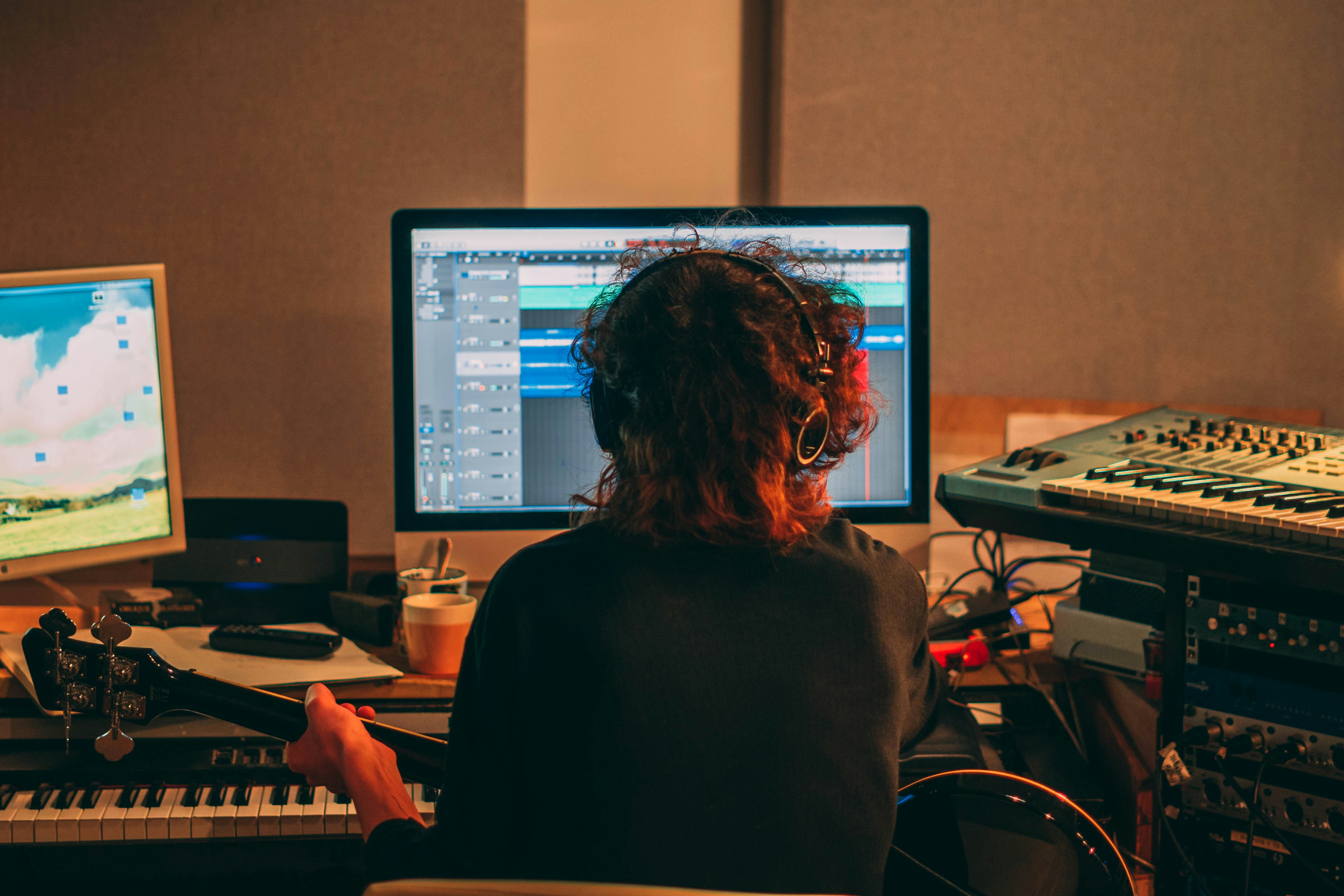 Person in headphones playing acoustic guitar in front of a recording studio setup