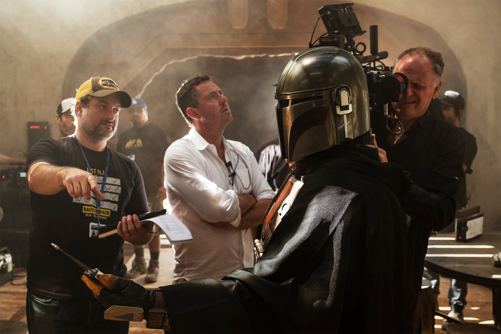 Filmmakers discussing a scene with a character costume in a dimly lit, rustic set.