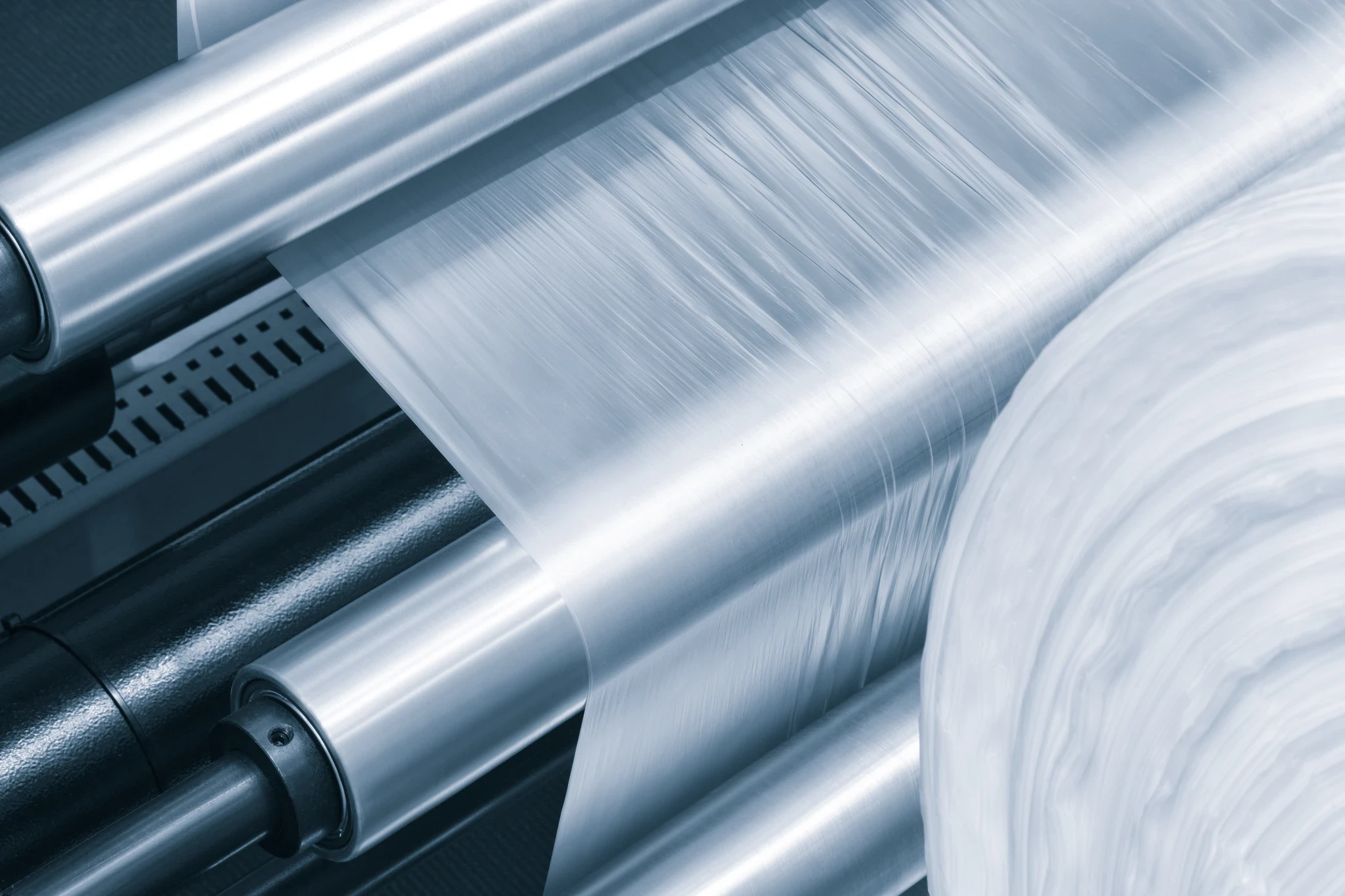 Rolls of clear plastic film running through the polished metal rollers of a production machine.