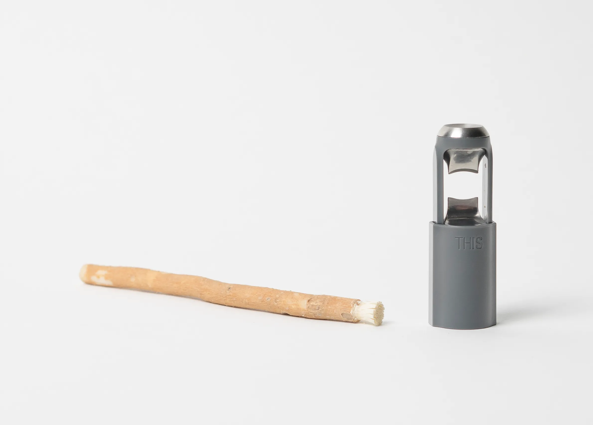 Gray THIS toothbrush housing displayed beside a natural miswak stick on white