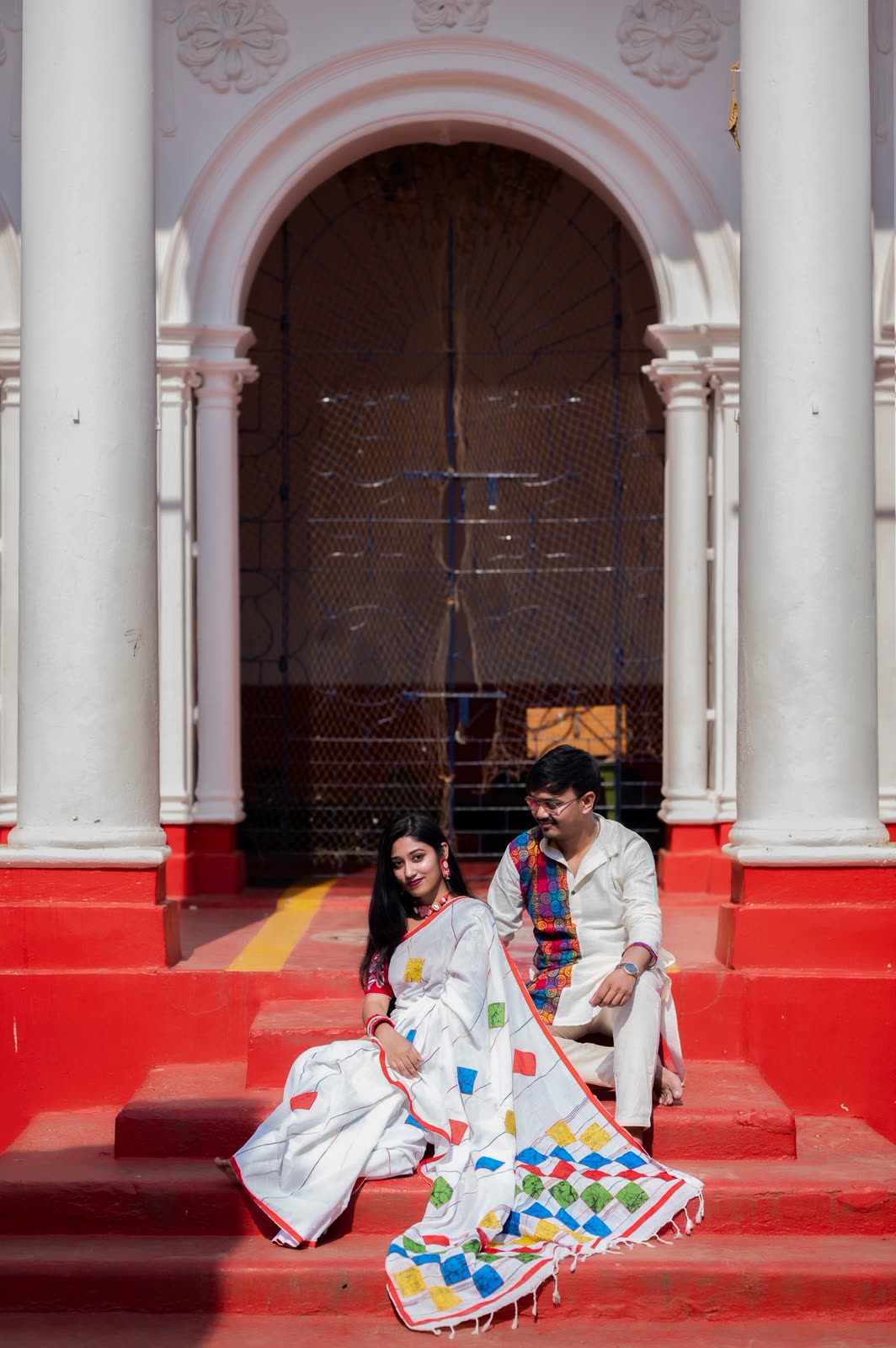 Couple sitting on bright red steps between white pillars