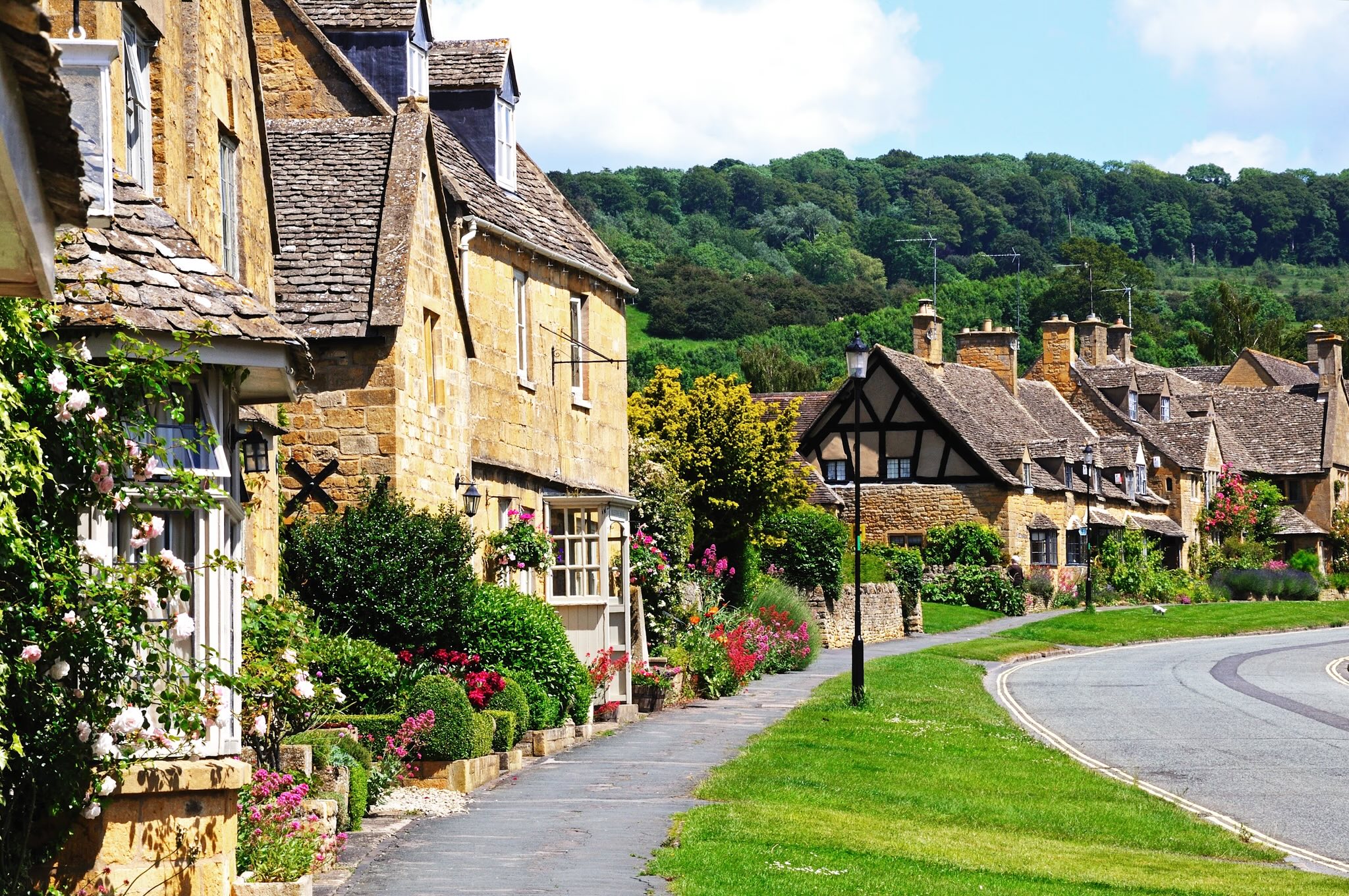 “Broadway High Street, Cotswolds, with golden stone cottages, landscaped gardens, and rolling countryside — symbolising luxury rural living and heritage estates in England.”