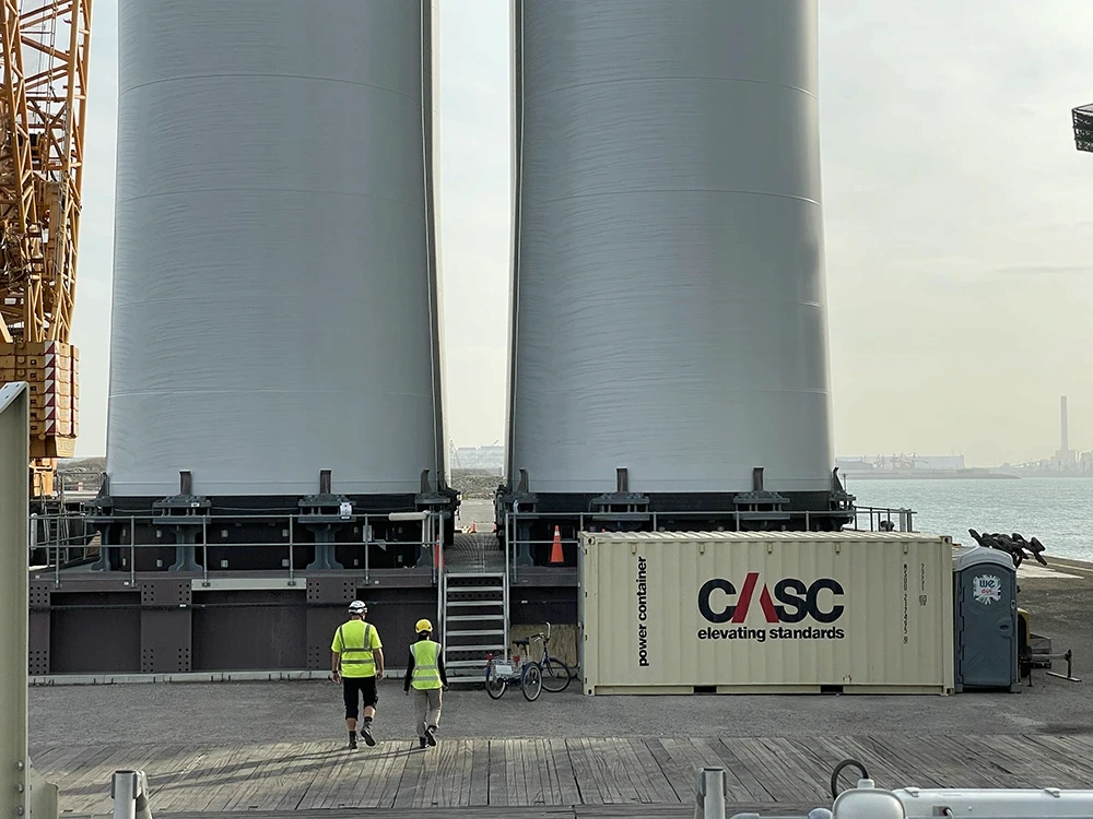 Site supervisors in PPE walking through an active construction site with cranes and wind turbines