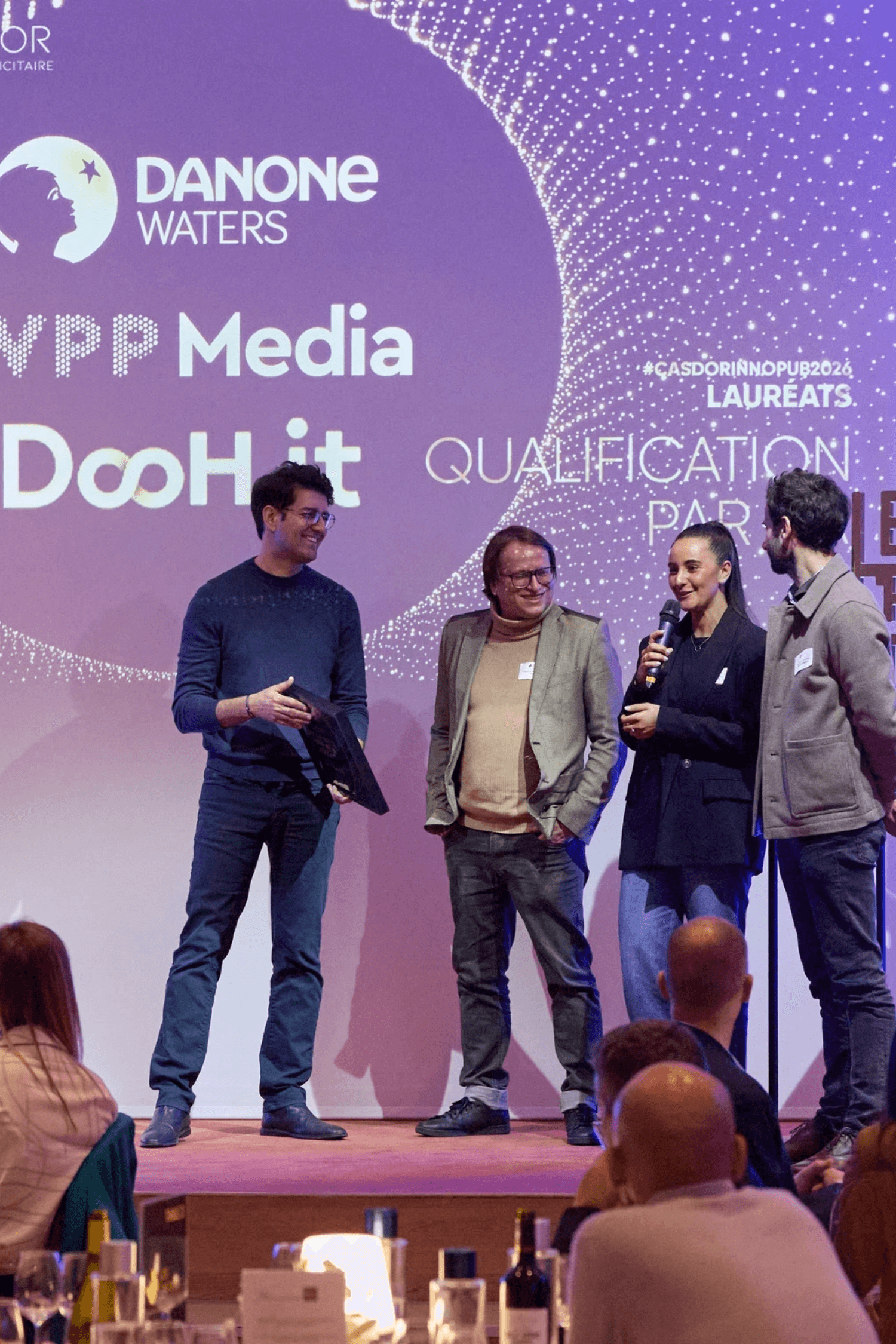 Two men in dress shirts stand against a striped background. One adjusts his tie, both look thoughtful and focused, conveying a professional tone.