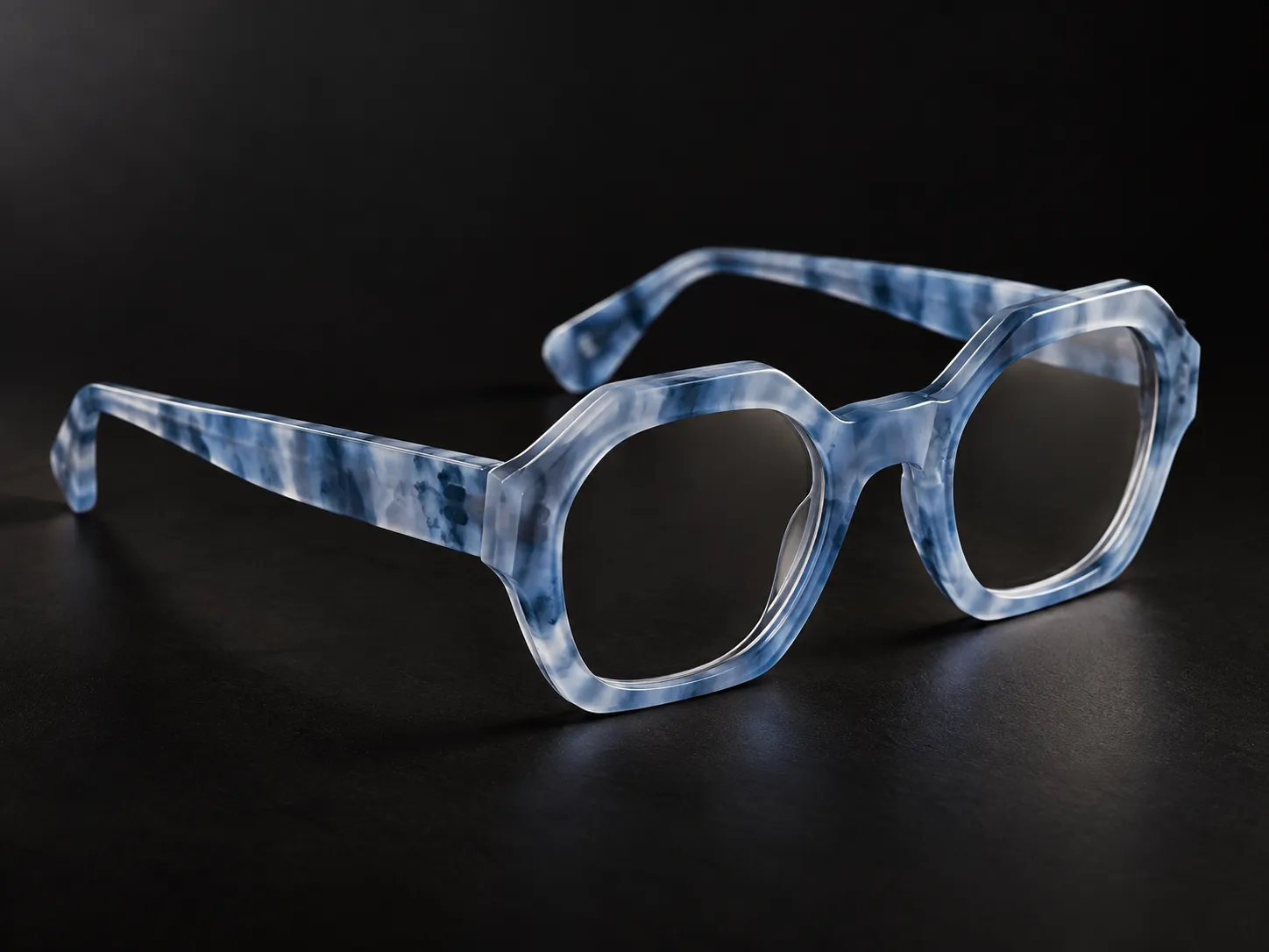 Occhiale IDIA realizzato in acetato di cellulosa blu marmorizzato, con struttura spessa, geometrica e lavorazione artigianale evidenziata dalla fotografia su fondo scuro. L’acetato è uno dei materiali disponibili per gli occhiali su misura IDIA di Ottica Dentella ad Ancona e permette di personalizzare colore, trasparenze, texture, forma e proporzioni della montatura.