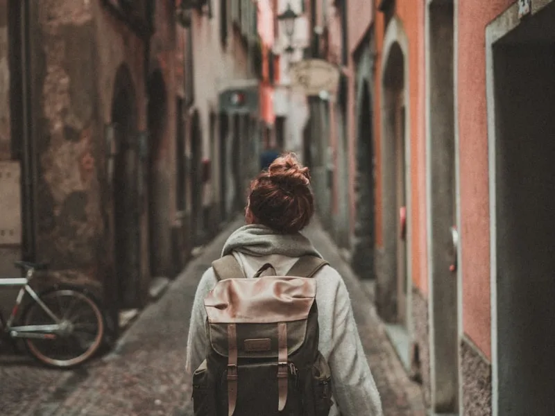 Жена с черна раница стои сред кафява пустиня