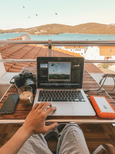 Person working remotely on a laptop from a sunny Mediterranean balcony