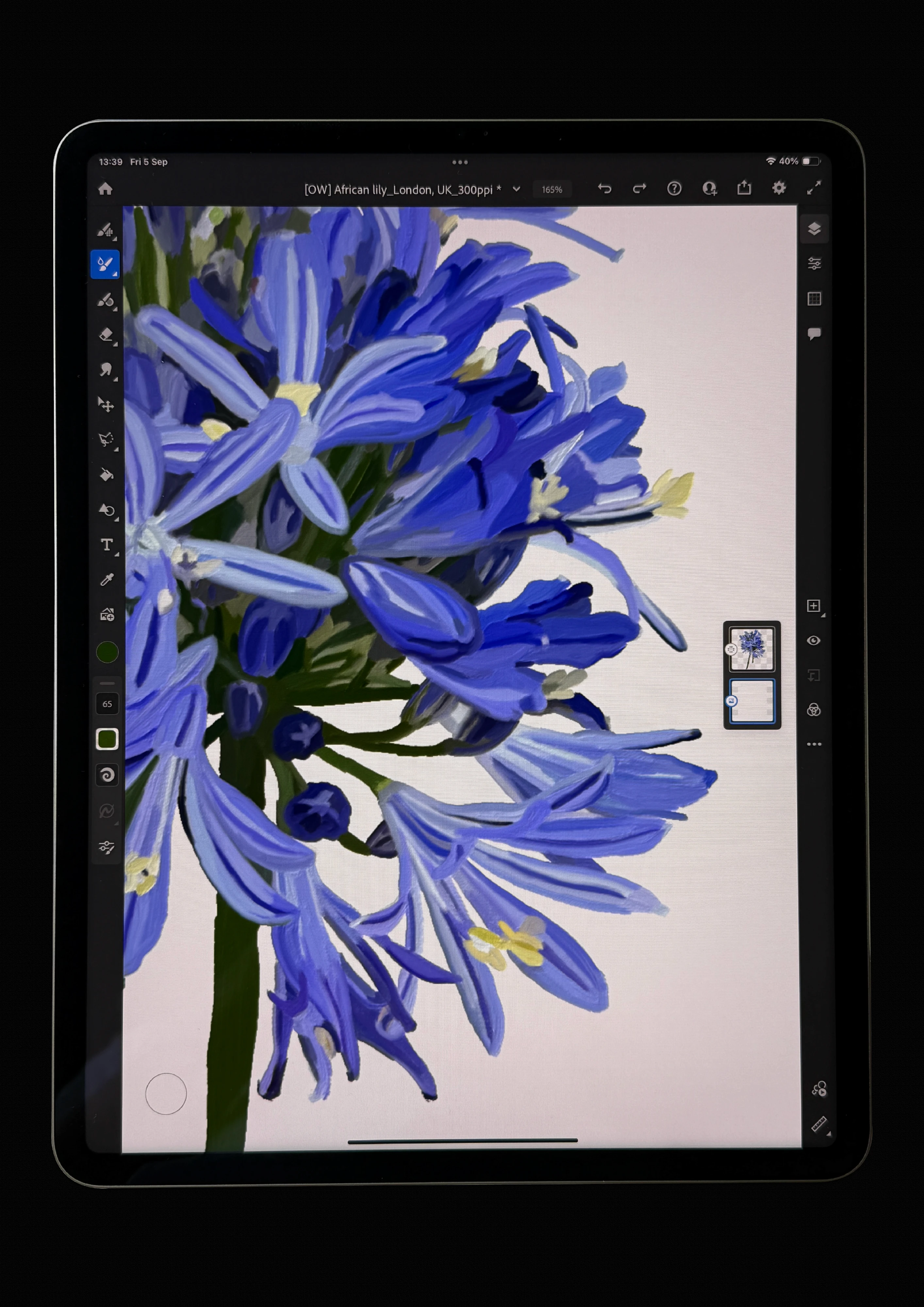 Tablet screen in a painting app showing a close, half-finished oil painting of blue lily flowers on a green stem.