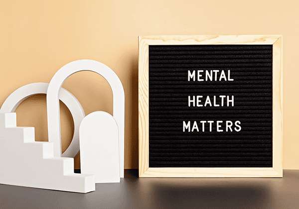 Black letter board with "MENTAL HEALTH MATTERS" in white text, displayed beside white arch decorations on a gray surface.