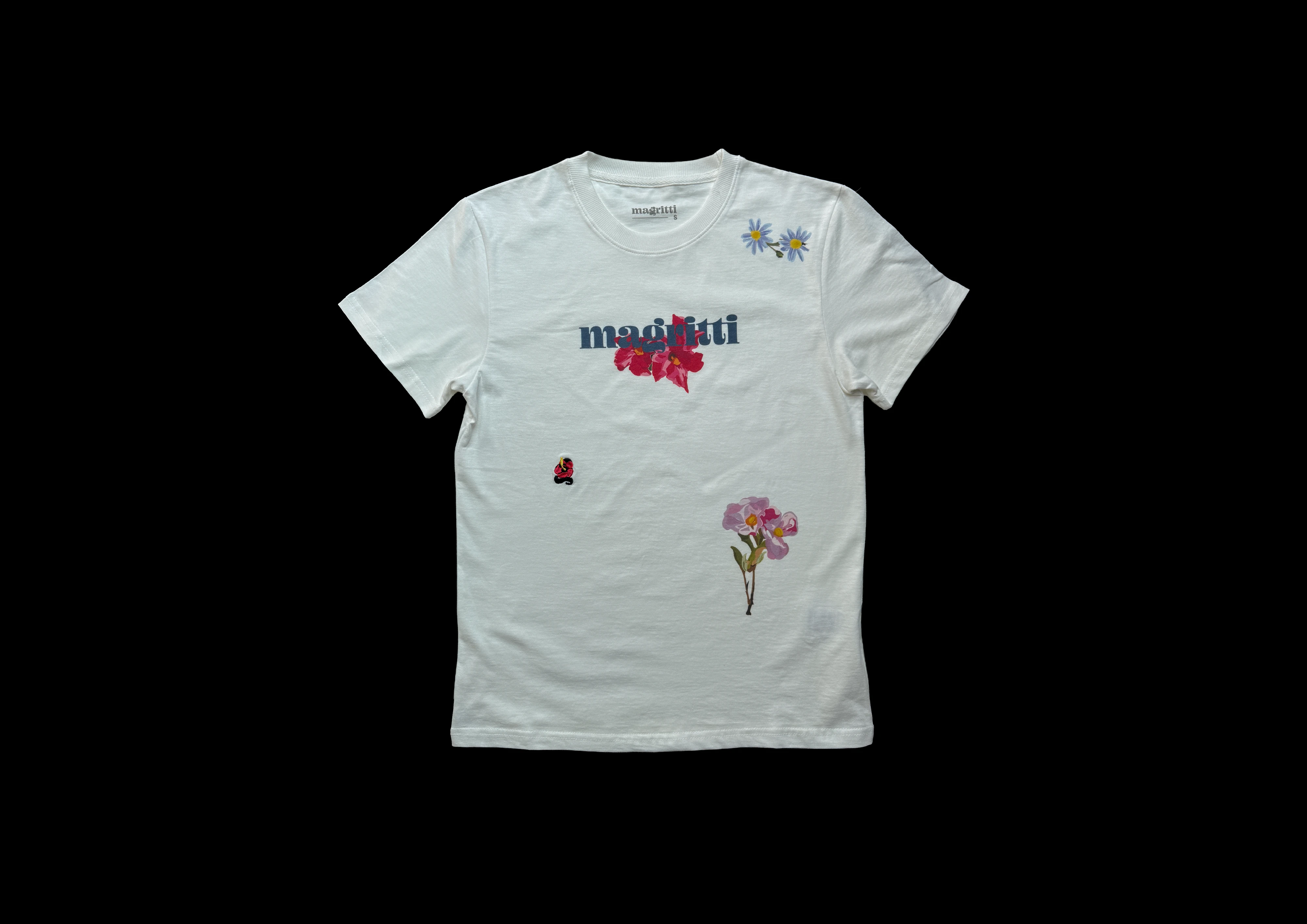 A white cotton shirt laid flat on black, showing four placements: daisies at the shoulder, a logotype with red flowers, a small embroidery, and pink flowers on the front body.