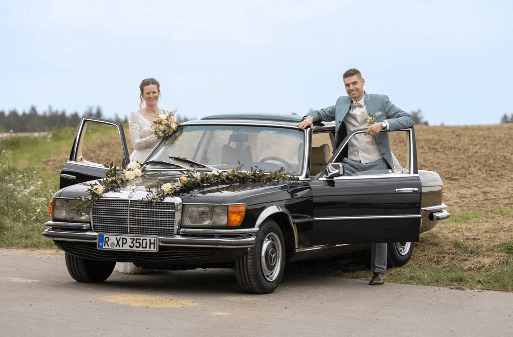 Brautpaar sitzt und steht auf Oldtimer während Hochzeitsshooting auf Feldstraße in Mallersdorf, Niederbayern