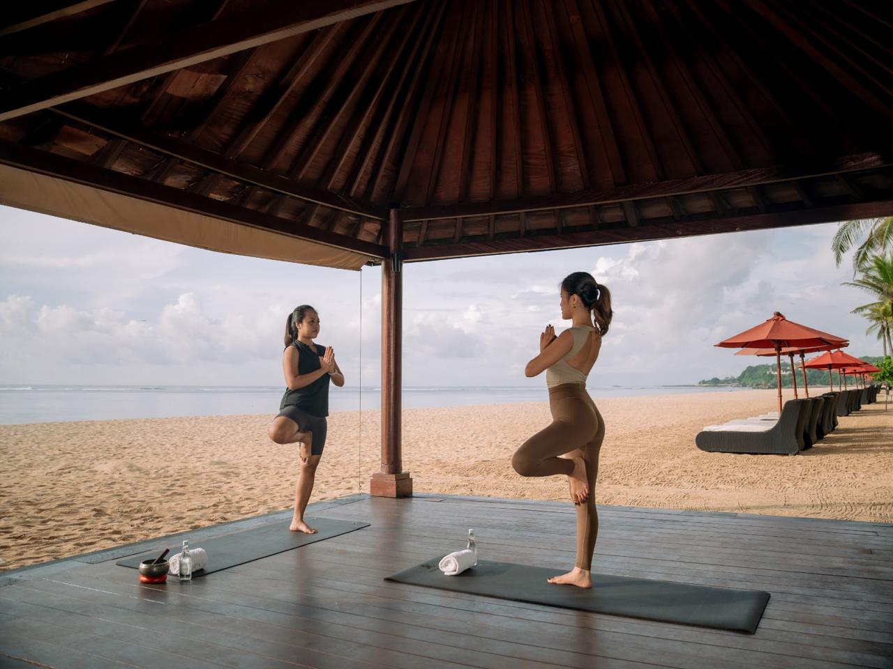 Wooden sauna cabin and hot tub set among rocky mountains and greenery under clear sky.
