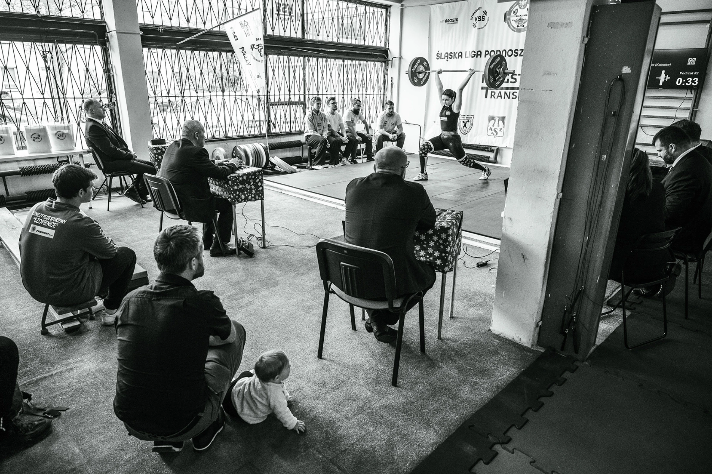 Jury patrzy jak młoda kobieta podnosi ciężar.