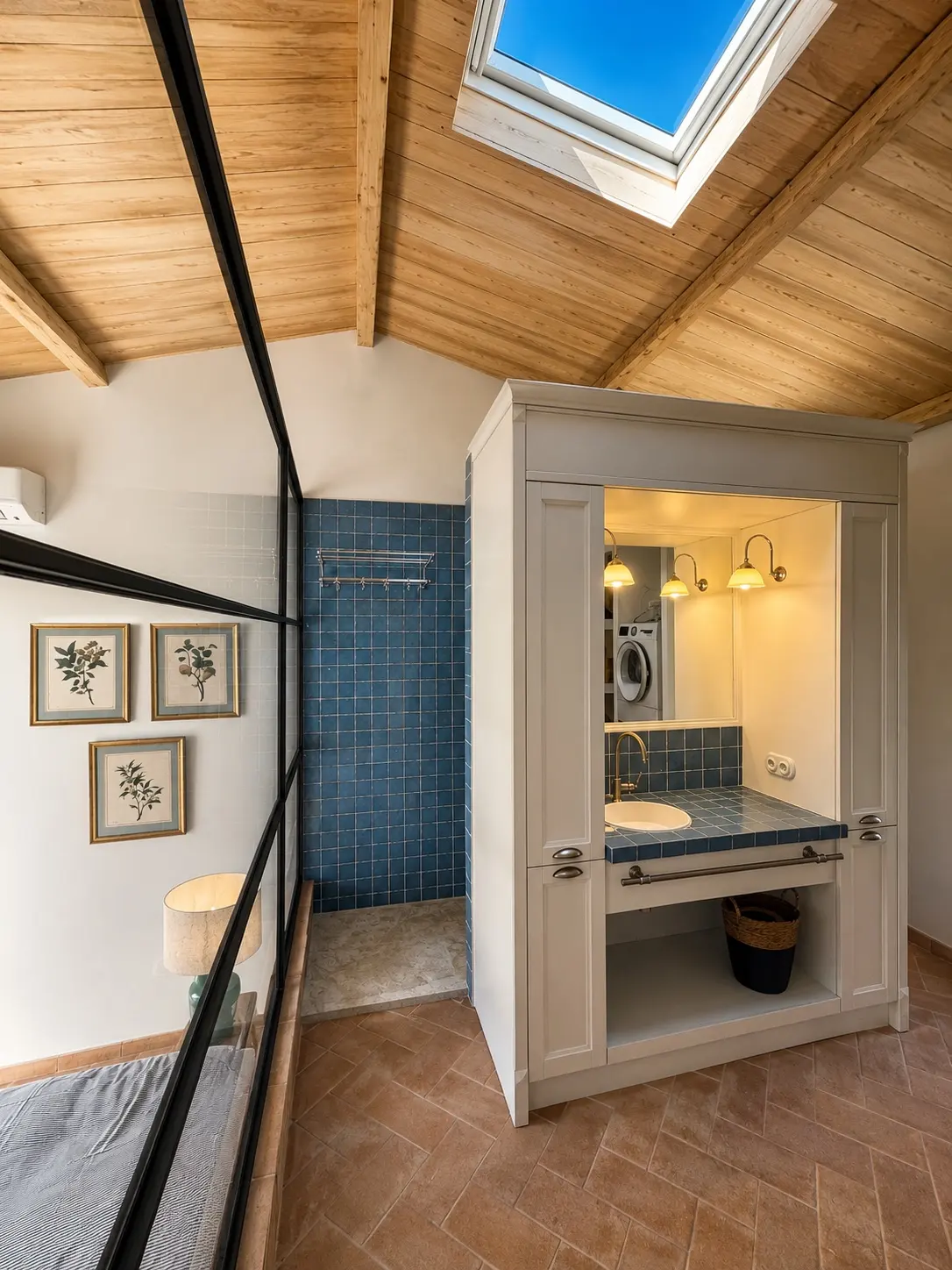 Salle de bain rénovée avec zellige bleu, charpente apparente et fenêtre de toit